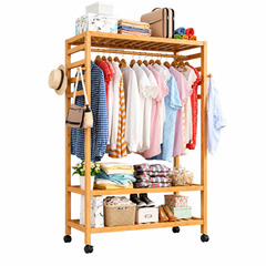 Bamboo rolling clothes rack with wheels, hanging rod, 3 slatted shelves and side hooks holding clothes, a hat and bags