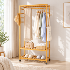 Natural bamboo 3-tier clothes rack with shirts on hangers, a scarf, handbag, basket and slippers beside a window