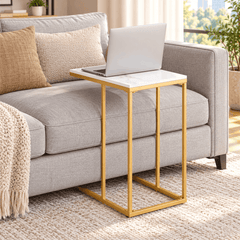 Gold frame C shaped table with a white top holding a laptop next to a grey sofa in a bright living room