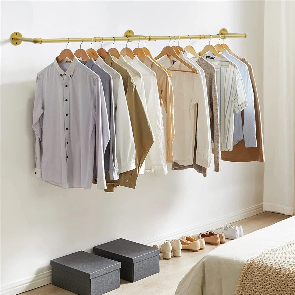 Gold wall mounted pipe clothes rack with shirts on wooden hangers above shoe boxes and shoes in a bedroom