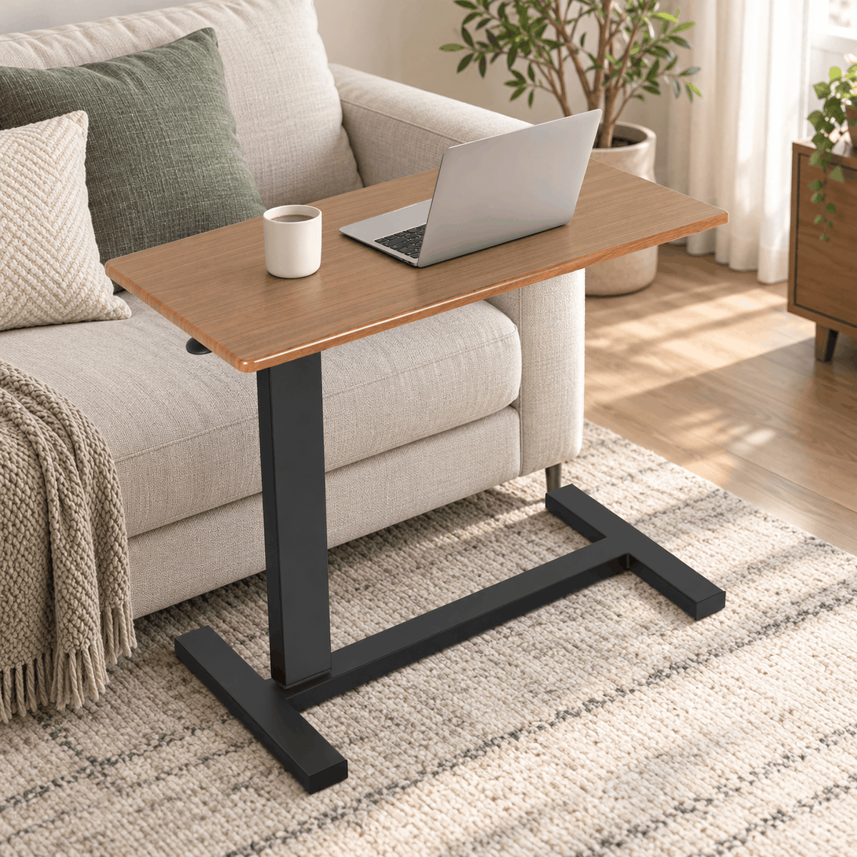 Height adjustable C shaped table with a wood look top next to a cream sofa holding a laptop and a mug