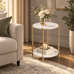 Round gold leg side table with two white marble look tops beside a cream sofa holding flowers, a candle and books