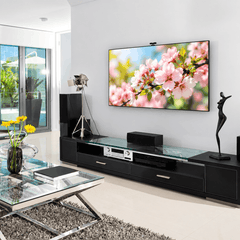 Wall mounted TV above a black TV unit with speakers and an amplifier in a bright living room with glass doors