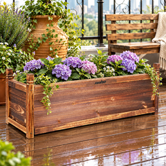 Wooden planter box with purple hydrangeas and ivy on a wet balcony deck beside a bench and terracotta pot
