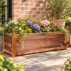 Wooden planter box with hydrangeas, daisies and ivy on a paved patio beside a red brick wall